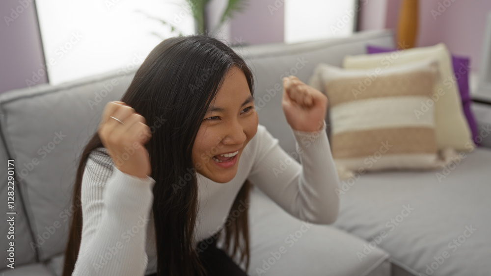 Young woman cheering excitedly in a cozy living room setting, expressing joyful emotion while seated on a comfortable sofa surrounded by soft cushions. Young woman cheering excitedly in a cozy living room setting, expressing joyful emotion while seated on a comfortable sofa surrounded by soft cushions.