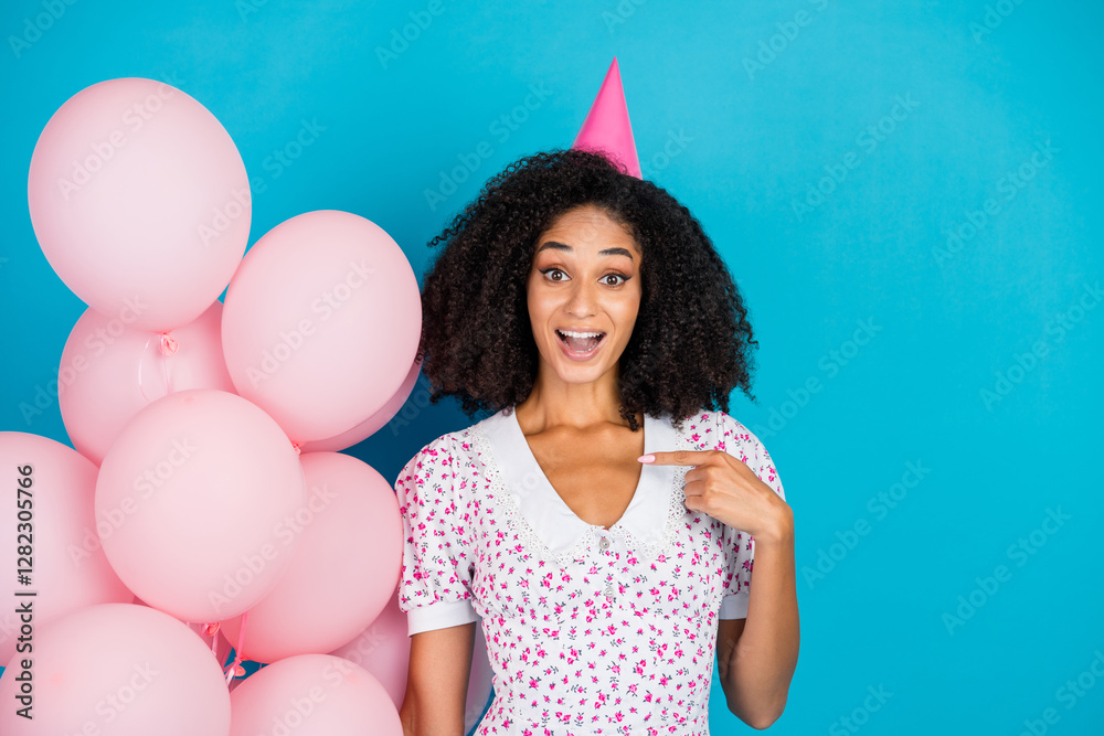 Fototapeta premium Cheerful Young Woman Celebrating in a Party Hat With Balloons, Wearing a Trendy Floral Dress Against a Vibrant Blue Background