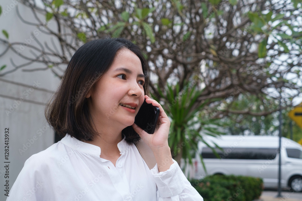 Young woman smiling while talking on phone outdoors, with greenery and urban background, capturing a moment of communication and modern connection. Young woman smiling while talking on phone outdoors, with greenery and urban background, capturing a moment of communication and modern connection.