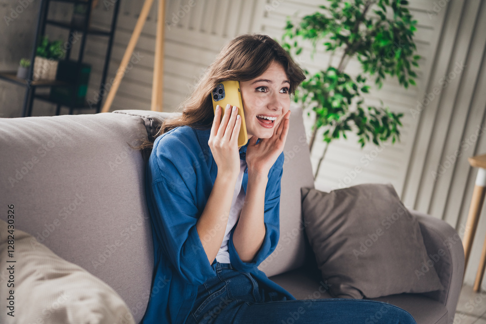 Happy young woman with brown hair talking on phone in stylish indoor living room setting Happy young woman with brown hair talking on phone in stylish indoor living room setting