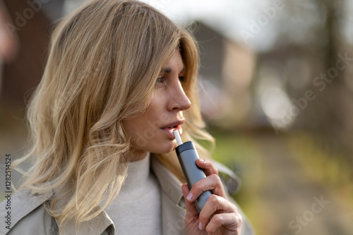 Young woman enjoying a moment outdoors while using a personal vaporizer on a sunny day