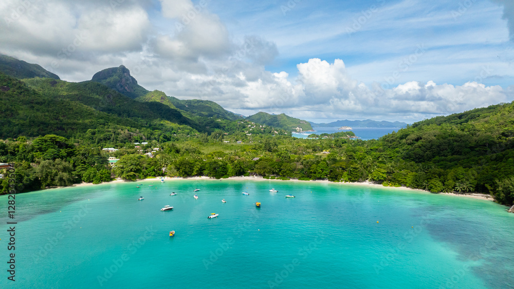 A picturesque turquoise bay with anchored boats and lush mountains in the background. Seychelles, Mahe. Port Launay. A picturesque turquoise bay with anchored boats and lush mountains in the background. Seychelles, Mahe. Port Launay.