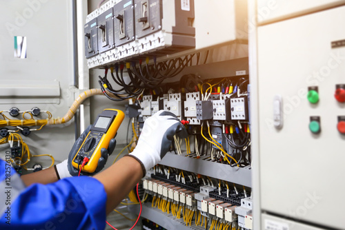 Electrical service technician holding electricity checking equipment to check electric current circuit breaker terminal panel and cable wiring main power distribution board for maintenance system.
