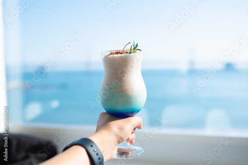 A young man is holding a glass with blue Hawaii Italian soda by the sea.
