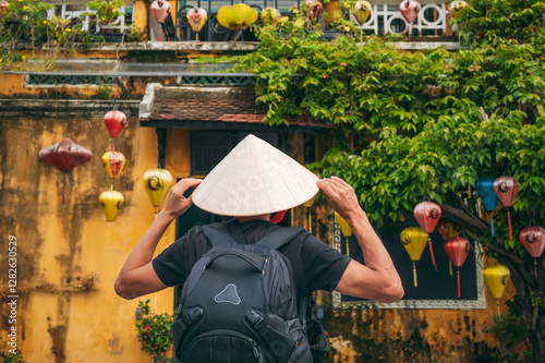 back of Asian male traveler tourist in traditional vietnamese hat on a street in old town in Hoi An city in Vietnam in Asia