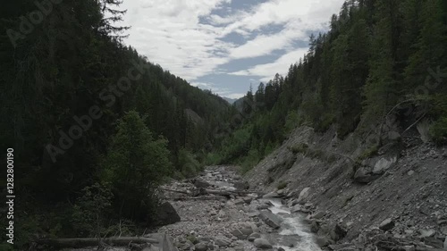 Rising-up drone footage of a stream flowing on the rocks in a forest canyon on the Alps