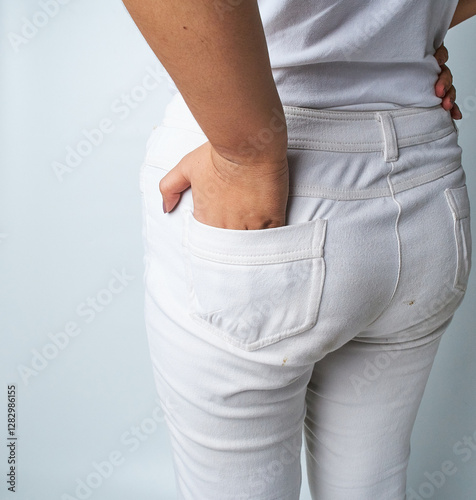 Person Wearing White Jeans Standing Against a Neutral Background With One Hand in the Pocket