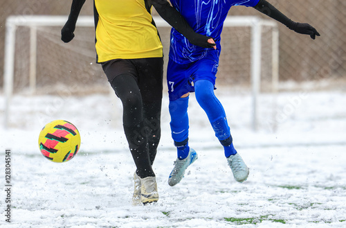 Two young football soccer players in a competitive match on a snow-covered field, showcasing intensity and athleticism in winter conditions.