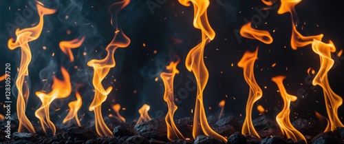 Abstract flames in various shapes and colors rising from black coal surface on dark background with smoke effects