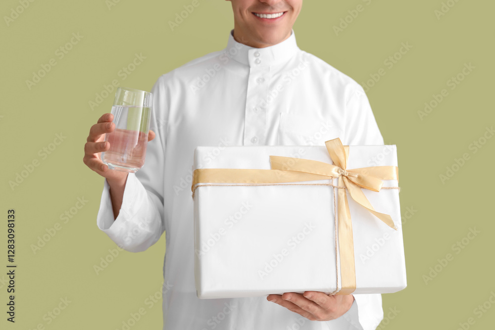 Young Muslim man with glass of water and gift box on green background, closeup. Ramadan celebration Young Muslim man with glass of water and gift box on green background, closeup. Ramadan celebration