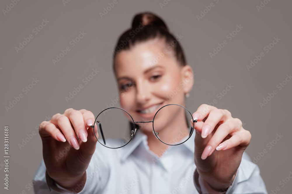 Smiling woman holding round eyeglasses in front of her, offering a clear vision concept, close-up shot. Smiling woman holding round eyeglasses in front of her, offering a clear vision concept, close-up shot.