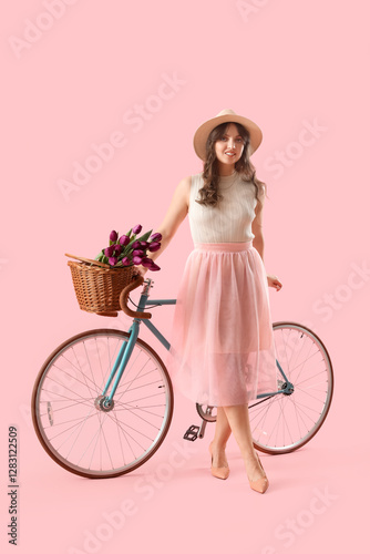 Pretty young woman with bicycle and bouquet of beautiful purple tulips on pink background photo