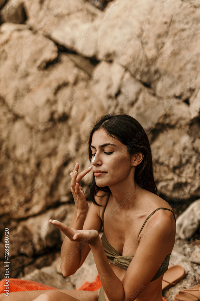 Smiling woman in a bikini applying sun lotion on a rugged seaside spot. Vacation mode concept Smiling woman in a bikini applying sun lotion on a rugged seaside spot. Vacation mode concept