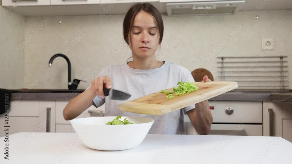 Cooking salad, teenage girl adding lettuce to the bowl, preparing a meal with fresh ingredients, modern home cooking Cooking salad, teenage girl adding lettuce to the bowl, preparing a meal with fresh ingredients, modern home cooking
