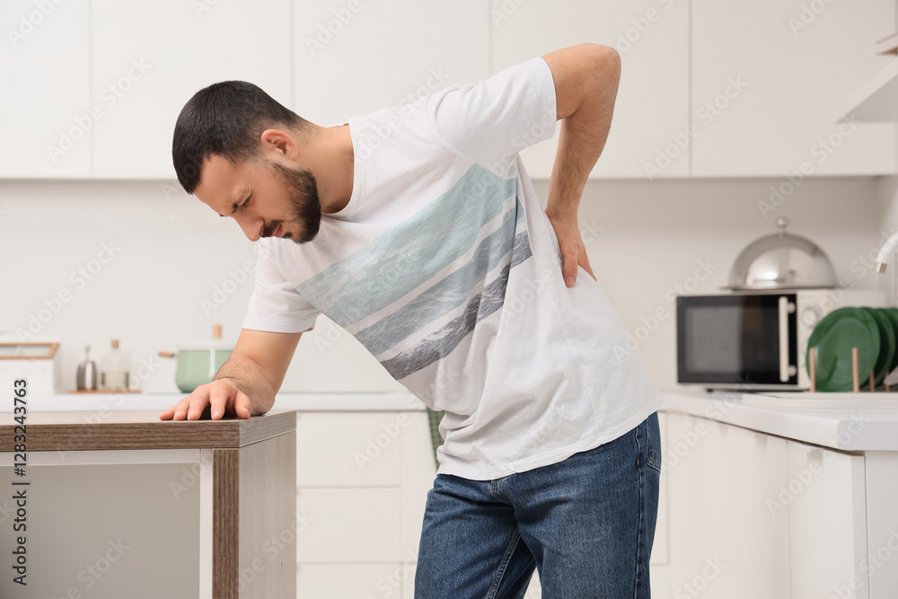 Young man suffering from back pain in kitchen Young man suffering from back pain in kitchen