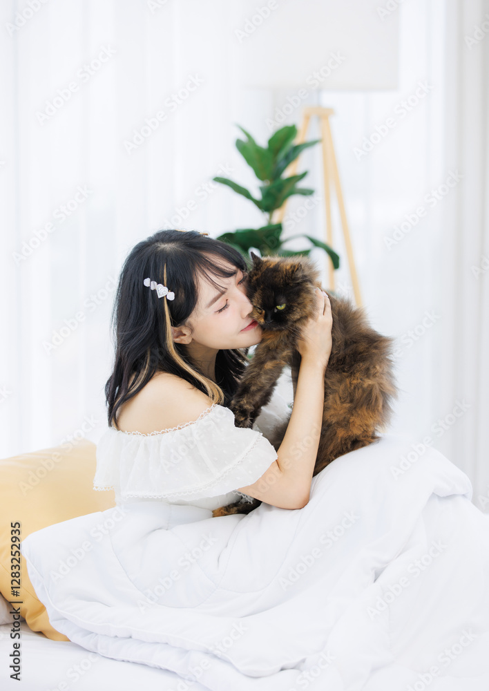 Obraz premium Asian happy young female sitting on white bed owner smiling hugging playing fluffy tortoiseshell cute little kitten breed pussycat pet friend in bedroom at home, Concept love animal comfort rest care.