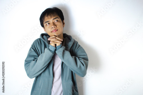 Asian teenager in white t-shirt and blue hoodie, posing hopefully with hands clasped