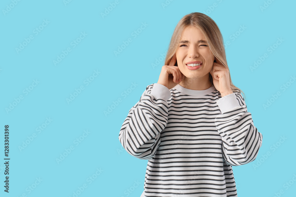 Young woman suffering from loud noise on blue background Young woman suffering from loud noise on blue background