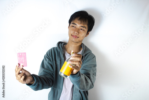 Asian teenager in white t-shirt and blue hoodie, posing showing his credit card and drinking glass