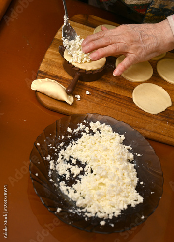 Obraz na płótnie Woman skillfully fills dough circles with cheese in a warm kitchen. w salonie