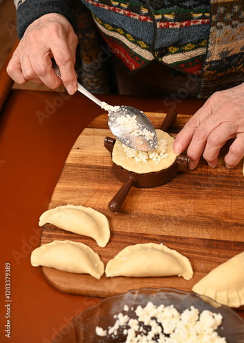 Obraz na płótnie Woman skillfully fills dough circles with cheese in a warm kitchen. w salonie