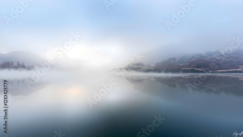 Wallpaper Mural A serene lake enveloped in fog reflects the surrounding mountains, creating a tranquil and ethereal atmosphere in soft, blue tones.   Torontodigital.ca