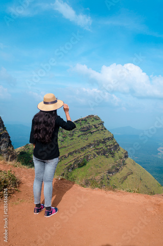 A female traveler  wearing a hat and posing by looking towards the view of Deviramma Betta in Chikkamagaluru, Karnataka, India photo