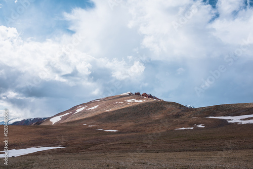 Sunlit snowy dome and sharp thorns on big hill top under clouds in blue sky. Rocky spikes on large mountain in sunlight. Thorny rocks in changeable weather. Spiky old stony outliers in high mountains. photo