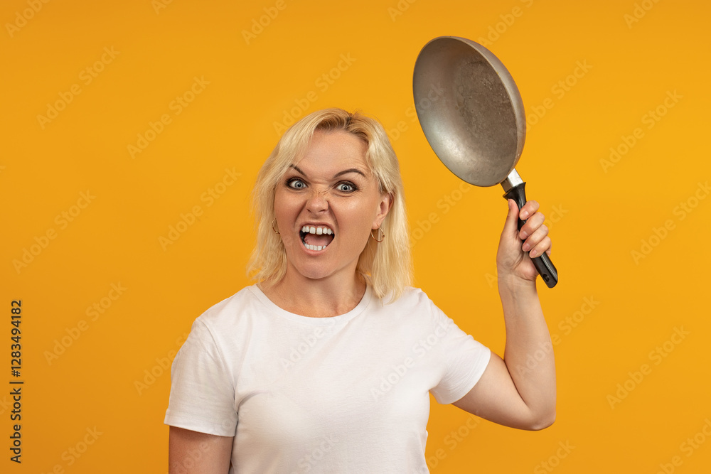 angry housewife with a frenzied face swings a frying pan towards the camera on a yellow background angry housewife with a frenzied face swings a frying pan towards the camera on a yellow background