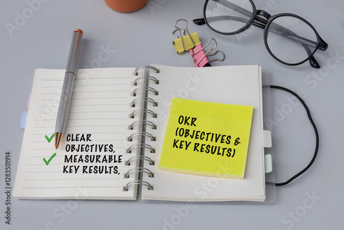 A top-view shot of a notebook labeled "OKR (Objectives & Key Results) Framework" placed next to a sticky note on a desk