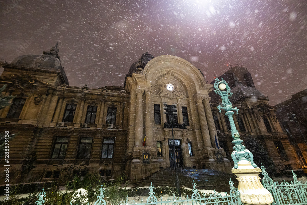 The historic CEC Palace in Bucharest covered in snow at night, with soft lighting highlighting its elegant architectural details. Winter in Bucharest.
