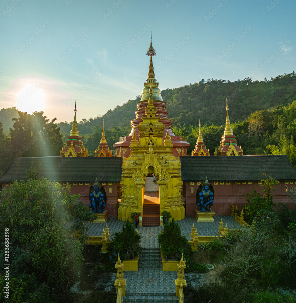 Naklejka premium aerial view of the golden gate with intricate golden architecture at Phra Yai Wat Phra That Doi Phra Chan (Daibutsu) temple..A stunning view of a traditional temple surrounded by lush greenery