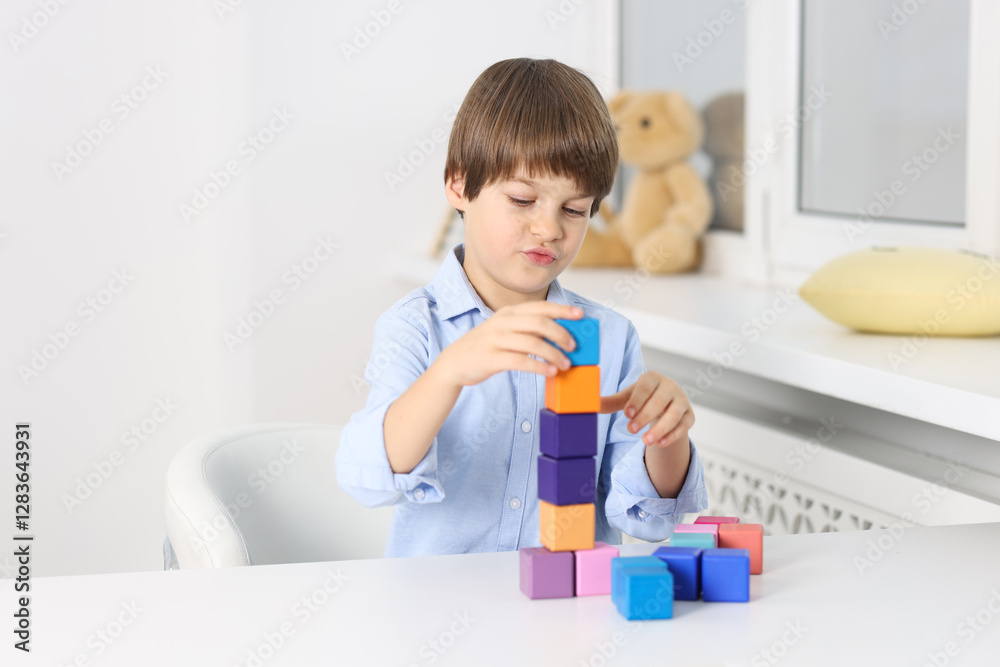 Boy building tower of colorful cubes at table indoors Boy building tower of colorful cubes at table indoors