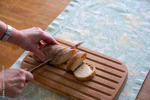 High angle view of wooden breadboard lying on oak table with women hands cutting bread with place setting background. Photo taken February 22nd, 2025, Zurich, Switzerland. photo