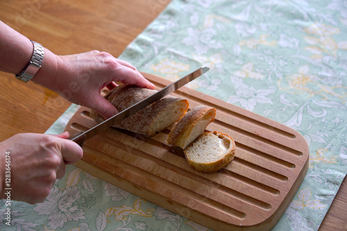 High angle view of wooden breadboard lying on oak table with women hands cutting bread with place setting background. Photo taken February 22nd, 2025, Zurich, Switzerland. photo