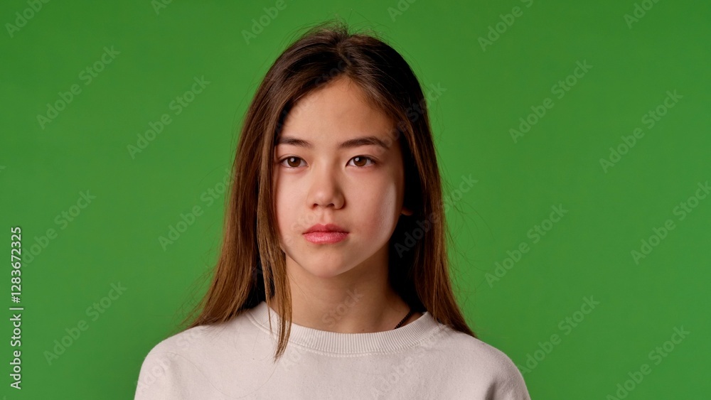 Obraz premium Asian girl child in shirt standing looking at camera, neutral expression, isolated on chroma key green screen studio background mockup.
