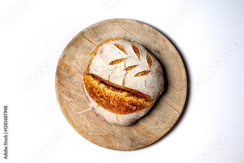 A homebaked artisan sourdough bread with scoring leaves on a round cutting board set on a pure white background.