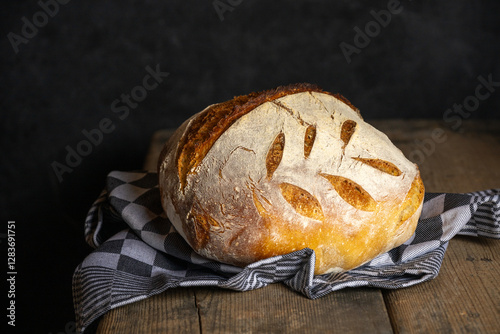 A homebaked artisan sourdough bread with scoring leaves on a teacloth.