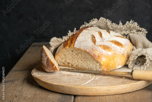 A cut homebaked artisan sourdough bread with a slice cut of and a breadknife on a round cutting board.