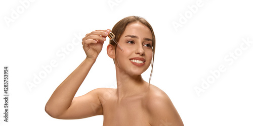 Smiling young woman applying skincare product, serum with dropper and looking sideways against white studio background. Concept of beauty and selfcare, hydration, nourishment, cosmetic. Ad photo