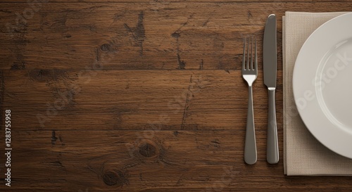 A high-angle, close-up view of a table . A white plate with a light beige linen napkin underneath it sits centered on the table. silver fork and knife, placed neatly beside the plate
