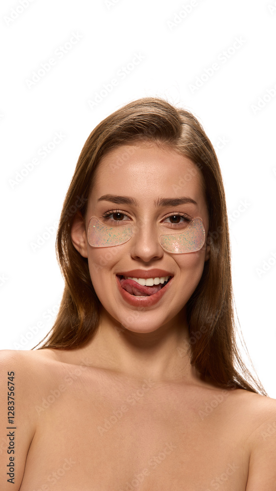 Portrait of young woman, with bare shoulders, sticking tongue out playfully while wearing under-eye patches against white background. Concept of natural beauty, hydration, freshness, wellness. Portrait of young woman, with bare shoulders, sticking tongue out playfully while wearing under-eye patches against white background. Concept of natural beauty, hydration, freshness, wellness.