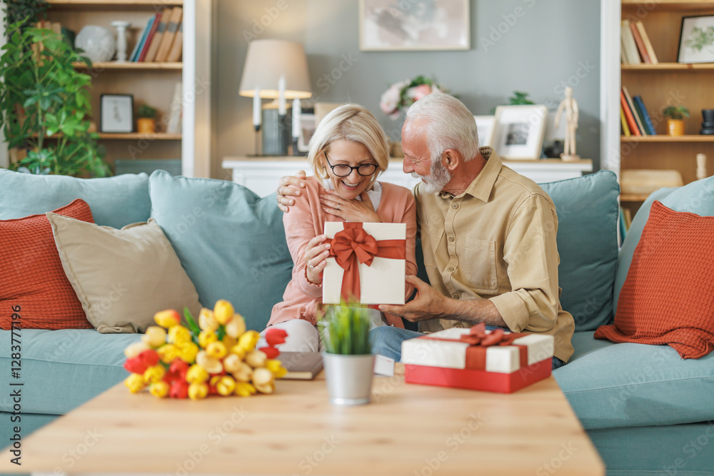 Couple sharing a joyful moment while opening a gift in a cozy living room decorated with flowers and warm colors Couple sharing a joyful moment while opening a gift in a cozy living room decorated with flowers and warm colors