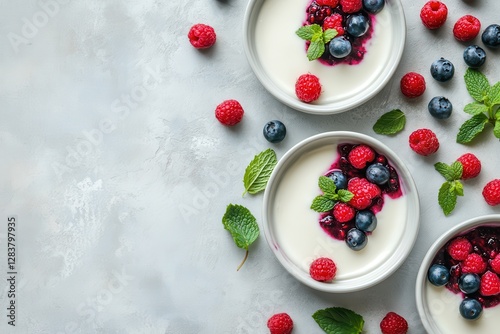 Delectable Panna Cotta Delight: Creamy Italian Dessert with Berry Sauce, Fresh Fruits, and Mint Garnish on a Stylish Gray Backdrop