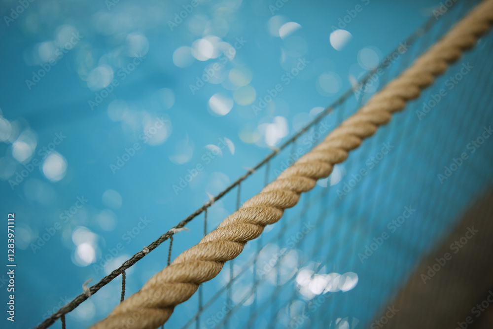 Fototapeta premium A fragment of rope fence with view at the sparkling water surface.
