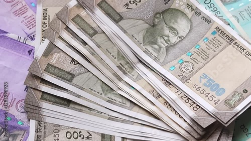 A person places a wad of 500 Indian rupee notes on a table surface on top of banknotes of different denominations. Top view slow motion video.