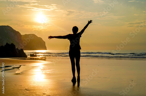 Silhouette of a woman on the beach at sunset doing gymnastics, exercising and running on the sand.