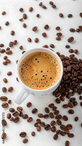 Overhead view of frothy espresso cup surrounded by coffee beans on white background. aromatic