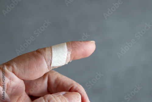 A close-up of a human finger wrapped with a small white bandage after a minor injury. 
