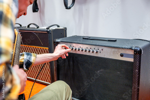 Guitarist adjusting settings on amplifier of electric guitar in recording studio